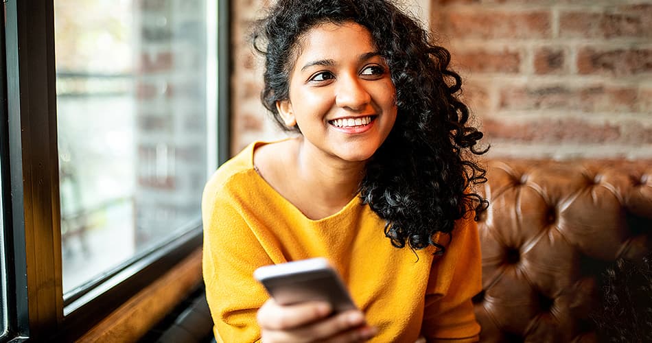 Lachende jonge vrouw zit op een bank en houdt een smartphone vast