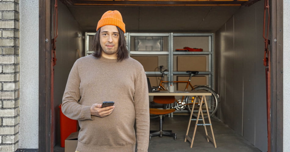 Man met oranje muts en smartphone in zijn hand staat voor een garage