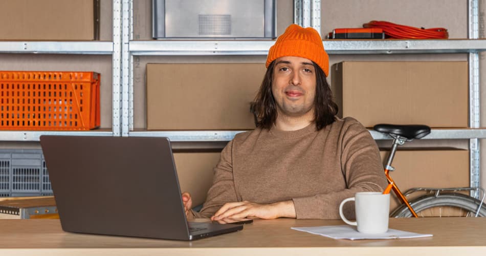 Man met oranje muts zit achter een laptop en glimlacht