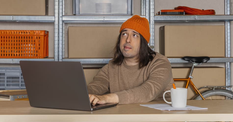 Man met oranje muts werkt op zijn laptop en denkt na