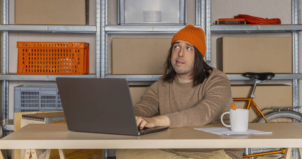Man met oranje muts werkt op zijn laptop en denkt na
