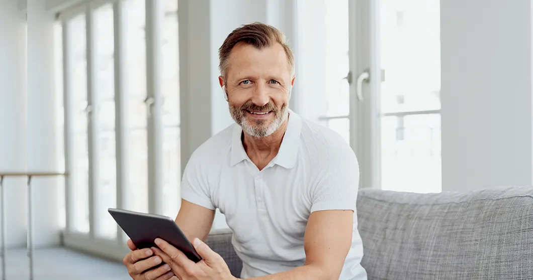 Man met tablet zit op de bank en glimlacht